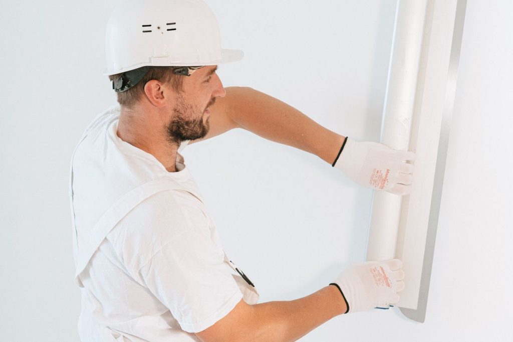 a-man-fixing-the-wall-4981812 Professional construction worker installing drywall with gloves and helmet inside a building.