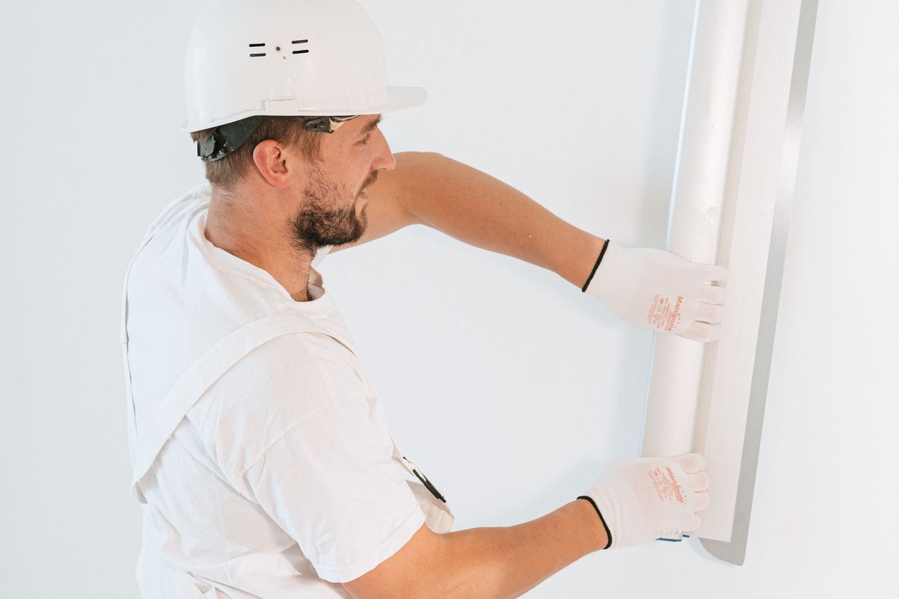 services-10 Professional construction worker installing drywall with gloves and helmet inside a building.