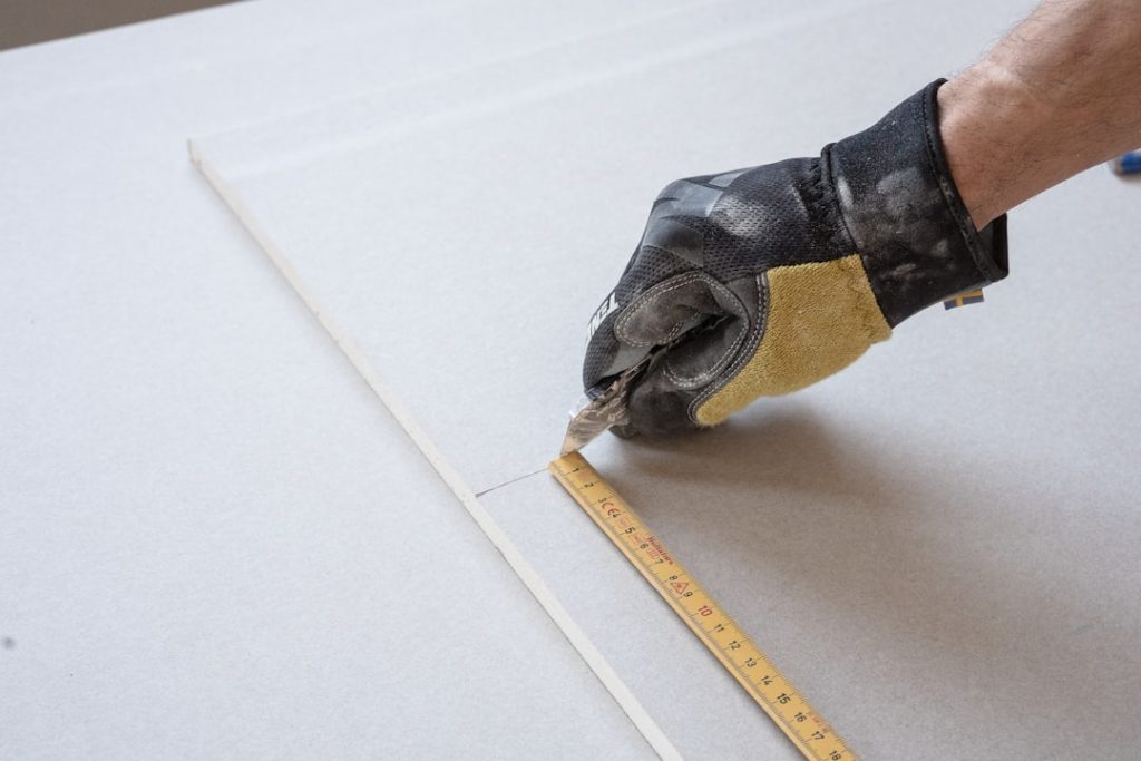 a-person-measuring-a-piece-of-paper-with-a-tape-lfdlrb2b2au A carpenter cuts a board with Ten Protection work gloves on.
