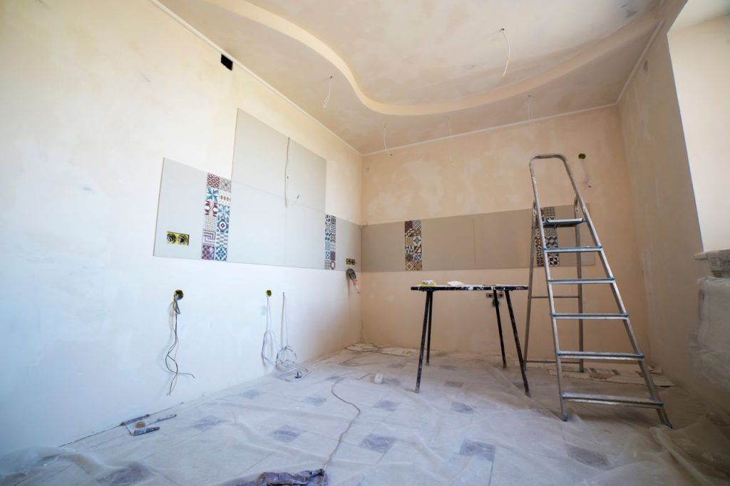modern-home-renovation-scene-with-ladders-36035072 Interior view of a room under renovation with paint, tiles, and tools.