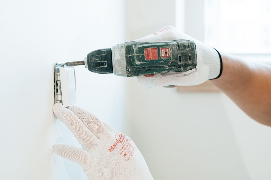 pexels-photo-4981794-4981794 Gloved hands using a drill to install a power outlet on a wall, focusing on precision and safety.